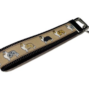 May include: A black and tan key chain with a silver key ring and a beige ribbon featuring a repeating pattern of colorful Collie dogs.