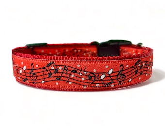 May include: Red dog collar with a white and black musical note pattern. The collar has white polka dots and a green buckle.