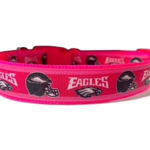 Op de afbeelding: Roze hondenband met een wit en zwart Philadelphia Eagles logo en helmdesign. De band heeft de tekst "Eagles" erop gedrukt.