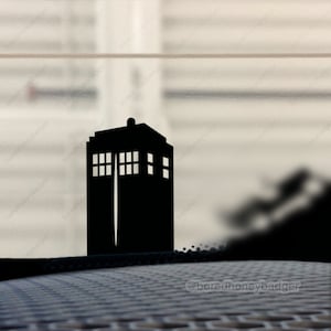 May include: A black silhouette of the TARDIS, the time machine from the Doctor Who television series, is on a car window. The TARDIS is a rectangular box with a rounded top and a door on the front. The TARDIS is a popular symbol of the Doctor Who franchise.