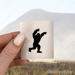 May include: A black silhouette of a gorilla with its arms raised in a threatening pose. The silhouette is printed on a white sticker.
