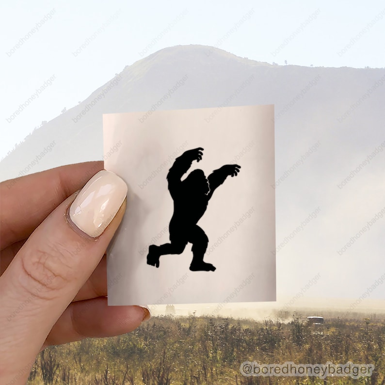 May include: A black silhouette of a gorilla with its arms raised in a threatening pose. The silhouette is printed on a white sticker.