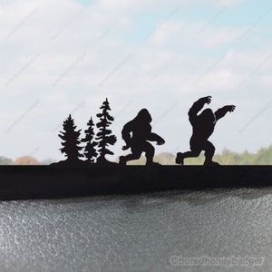 May include: Silhouette of two Bigfoot figures walking through a forest. The figures are black and are set against a blurry background of trees and a blue sky.