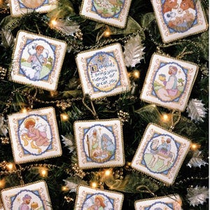 May include: A collection of square, cross-stitched Christmas ornaments. Each ornament features a different biblical scene or figure, framed with a blue border and gold trim. The ornaments are hanging on a Christmas tree.