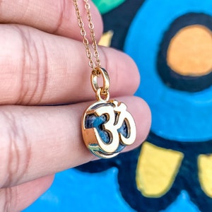 May include: A gold necklace with a pendant featuring the Om symbol. The pendant is made of gold and has a blue and white stone inside.