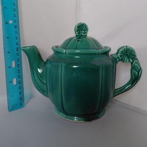 May include: A teal ceramic teapot with a lid and handle. The teapot has a ribbed design and a floral motif on the lid and handle. The teapot measures approximately 7 inches in height.