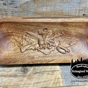 May include: A wooden serving tray with a carved design of a military insignia. The tray is brown and has leather straps on the sides. The text "Handcrafted Reimagined Wood Since 2009 www.ReimaginedWood.com" is on the bottom of the tray.