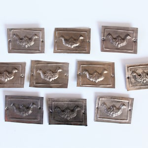 May include: Ten antique silver-toned metal plaques with a decorative floral design. Each plaque has a raised design of a stylised floral motif.