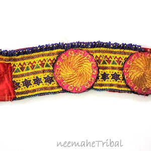 Könnte beinhalten: Ein rotes, gelbes, blaues und goldenes Perlenhaarband mit drei rosa und goldenen gestickten Kreisen. Das Haarband ist mit einem geometrischen Muster verziert.