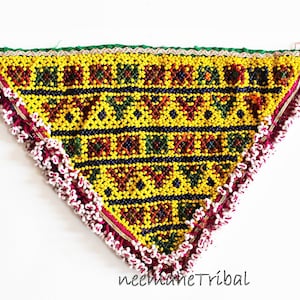 Puede incluir: Una bolsa triangular de cuentas con un patrón geométrico amarillo, rojo, verde y azul. La bolsa tiene un borde de flecos blanco y rojo.