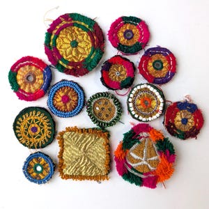 Può includere: Una collezione di abbellimenti tessili colorati e fatti a mano. I pezzi presentano ricami intricati, perline e frange in varie forme circolari e quadrate. I colori includono oro, rosso, verde, blu e rosa.