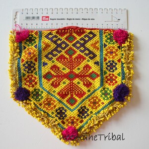 May include: A colorful beaded pouch with a geometric pattern in shades of yellow, red, green, blue, and purple. The pouch has a fringe border and pom-poms.