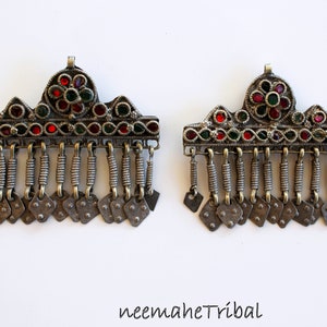 May include: A pair of silver hair clips with red and green glass stones. The clips have a decorative design with a flower in the center and a fringe of small silver beads.