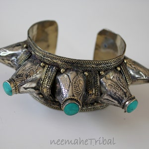 Può includere: Braccialetto in argento e ottone con pietre turchesi e un design decorativo. Il braccialetto ha una fascia larga con una serie di sporgenze appuntite, ciascuna sormontata da una pietra turchese.