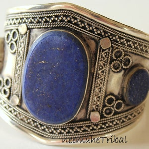 Può includere: Braccialetto in argento con disegni intricati e tre pietre ovali di lapislazzuli. Le pietre sono di colore blu scuro con una texture punteggiata.