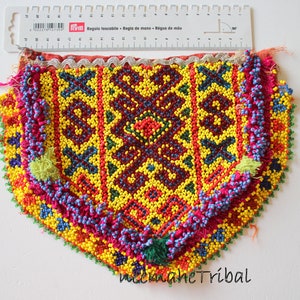 May include: A colorful beaded pouch with a geometric pattern. The pouch is made of small, colorful beads sewn together in a intricate design. The pouch has a fringe border and a white lace trim.