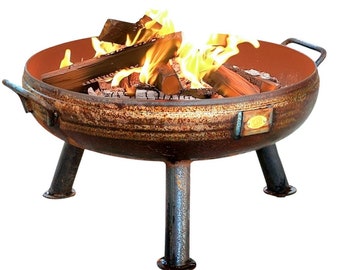 May include: A round, rusted metal fire pit with three sturdy legs and two side handles. The bowl features a smooth, reddish-brown interior and contains burning logs with bright yellow and orange flames flickering above the wood and charcoal.