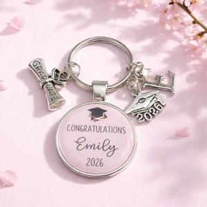May include: A silver graduation keyring with several charms. The main charm is a round pendant with the text "Congratulations Emily 2026". Additional charms include a graduation cap, diploma, and the letters "LE".