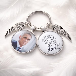 May include: Silver keyring with two round pendants and wing charms. One pendant shows a photo of a man, the other has the text "I have an ANGEL in heaven. CALL HIM Dad."