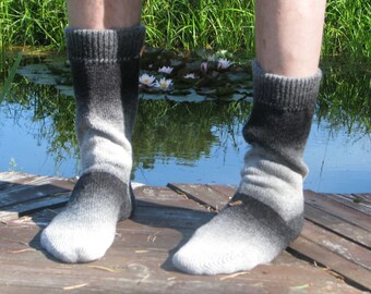 May include: A pair of black and white gradient socks with a ribbed cuff. The socks are worn by a person standing on a wooden dock over a pond with lily pads.