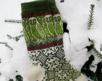 May include: A pair of green and white knitted socks with a red and white stripe pattern. The socks are lying on a bed of snow-covered evergreen branches.
