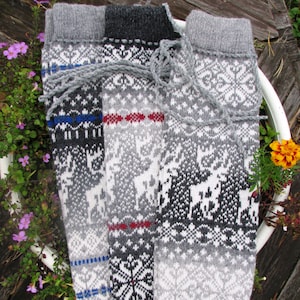 May include: Three pairs of knitted leg warmers in grey, black and white with a traditional Scandinavian pattern. The leg warmers are folded and displayed on a white surface.