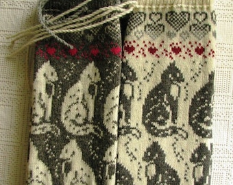 May include: Two knitted leg warmers with a cat pattern. One is dark gray with cream-colored cats, the other is cream-colored with dark gray cats. Both have red accents and a heart pattern.