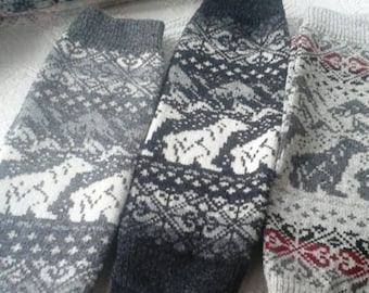 May include: Three pairs of knitted leg warmers with different patterns. One pair is black and white with a geometric design, another is grey and white with a geometric design, and the third is grey with a red and white geometric design.