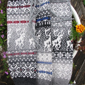May include: Three pairs of grey and white knitted leg warmers with different patterns. The leg warmers have a traditional Scandinavian design with reindeer and geometric patterns.
