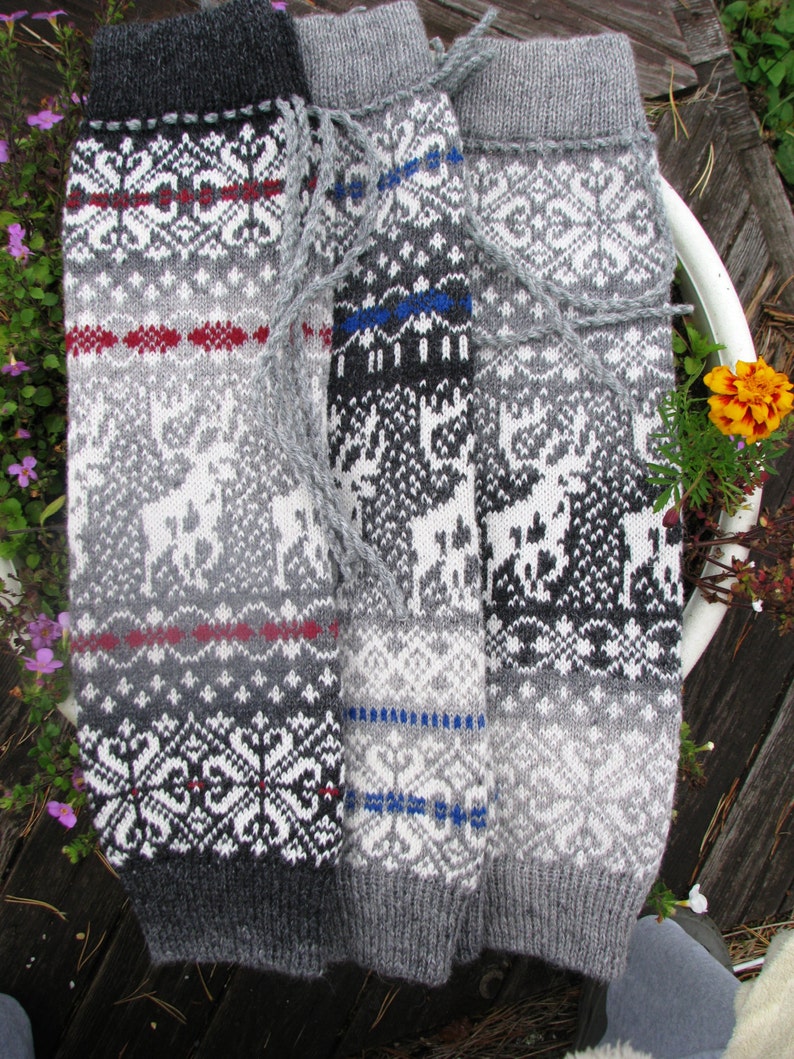 May include: Three pairs of grey and white knitted leg warmers with different patterns. The leg warmers have a traditional Scandinavian design with reindeer and geometric patterns.