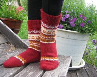Könnte beinhalten: Ein Paar rote Wollsocken mit weißen und orangefarbenen geometrischen Mustern. Die Socken werden von einer Person getragen.