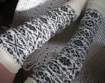 May include: A pair of white and black patterned leg warmers. The leg warmers are made of a soft, knitted fabric and have a geometric design.
