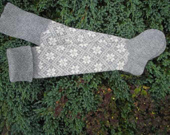 May include: A pair of gray knitted socks with a white diamond pattern. The socks are folded and lying on a green surface.