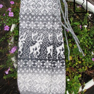 May include: Grey and white knitted leg warmers with a geometric pattern and a white background. The leg warmers have a fringe detail at the top.