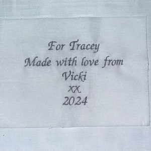 May include: White fabric with a grey embroidered message that reads "For Tracey Made with love from Vicki xx 2024".