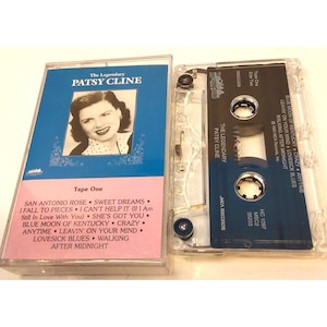 Op de afbeelding: Een cassettebandje met een verzameling liedjes van Patsy Cline. De cassetteband is in een doorzichtige plastic cassette met een blauw-wit label. Het label toont een foto van Patsy Cline en de titel "The Legendary Patsy Cline". De cassetteband bevat liedjes zoals "San Antonio Rose", "Sweet Dreams", "I Fall to Pieces", "I Can't Help It", "She's Got You", "Blue Moon of Kentucky", "Crazy", "Anytime", "Leavin' on Your Mind", "Lovesick Blues", "Walking After Midnight".