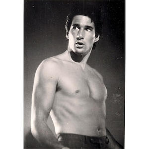 May include: A black and white photo of a man with a bare chest and a serious expression. He is looking up and to the right. He is wearing dark pants.