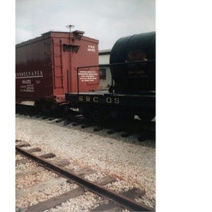 Könnte beinhalten: Ein roter Güterwagen mit der Aufschrift "Pennsylvania 96451" und "SRC OS" an der Seite. Der Güterwagen ist mit einem schwarzen Kesselwagen gekoppelt.