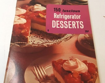 May include: A vintage cookbook cover featuring a pink background with the title "150 Luscious Refrigerator Desserts" in white text. The cover features a photo of a strawberry dessert with whipped cream and a fork on a white plate.