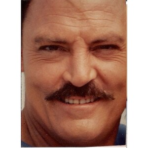 May include: A close-up of a man's face with a mustache and a smile. He has wrinkles around his eyes and a light complexion.