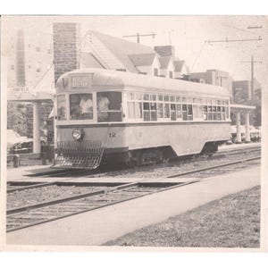 May include: A black and white photo of a vintage trolley car with the words "Moreland Boulevard" on the side. The trolley is numbered 12 and is stopped at a station.
