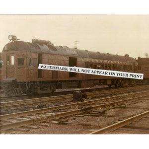 Może przedstawiać: Zdjęcie w odcieniach sepii przedstawiające wagon pasażerski Pennsylvania Railroad. Brązowy wagon ma ciemny dach, liczne okna i napis "PENNSYLVANIA" wzdłuż boku. Pociąg stoi na torach kolejowych.