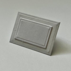 Puede incluir: Una tarjeta blanca con un marco rectangular en relieve. El marco tiene tres capas, creando un efecto de profundidad sutil.