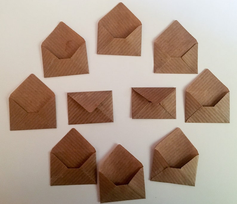 Puede incluir: Diez sobres de papel marr&oacute;n de diferentes tama&ntilde;os, dispuestos en semic&iacute;rculo sobre un fondo blanco.