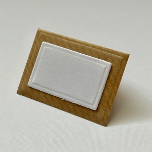 Puede incluir: Una tarjeta marr&oacute;n con un inserto rectangular blanco. La tarjeta tiene una superficie texturizada.
