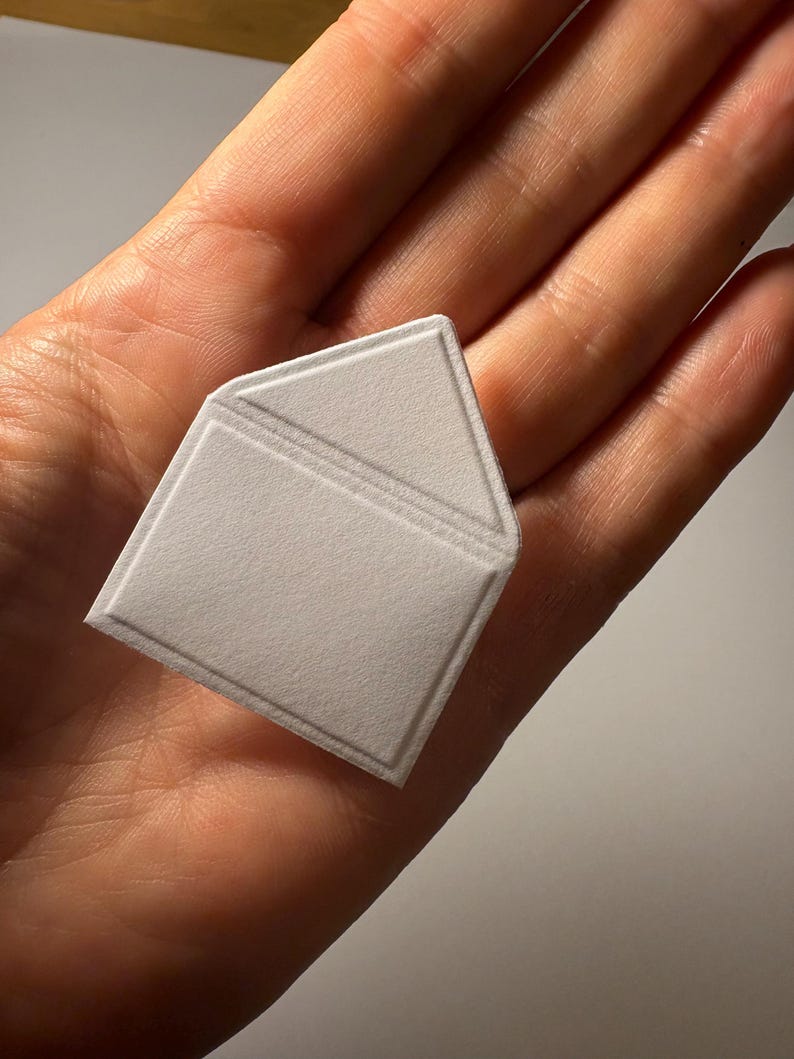 Puede incluir: Un sobre de papel blanco con una solapa doblada. El sobre es texturizado y tiene un dise&ntilde;o ligeramente en relieve.