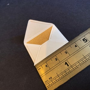 Puede incluir: Un sobre de papel blanco con una solapa de papel marr&oacute;n, medido con una regla que muestra 1 pulgada (2,5 cm).