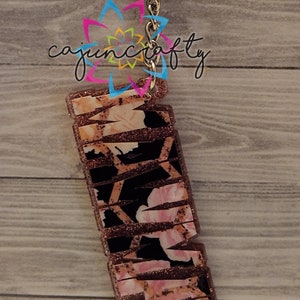 May include: A rectangular keychain with a floral and black pattern, accented with glitter. The keychain is attached to a silver keyring and chain. The text "cajuncrafty" is visible in the image.