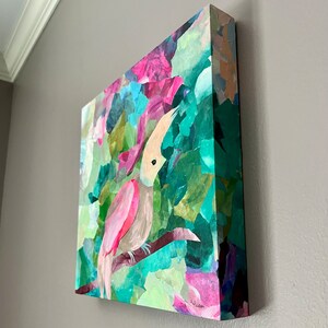 May include: A pink and gray toucan with a long beak is perched on a branch in a colorful jungle scene. The painting is made with paper scraps and has a textured, collage-like appearance.