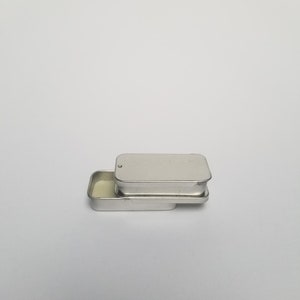 May include: A silver metal tin with a hinged lid. The tin is open and the inside is empty.